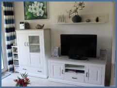 Der Wohnbereich ist modern und besitzt eine komfortable Sitzecke und einem bequemen Sessel. Ein Flachbildfernseher und eine Musikanlage in einer hellen Wohnwand runden das Bild ab.